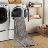Laundry room scene with black and gray Consuelo Washable Area Rug coming out of the dryer on top of a jute rug. Washing-Machine