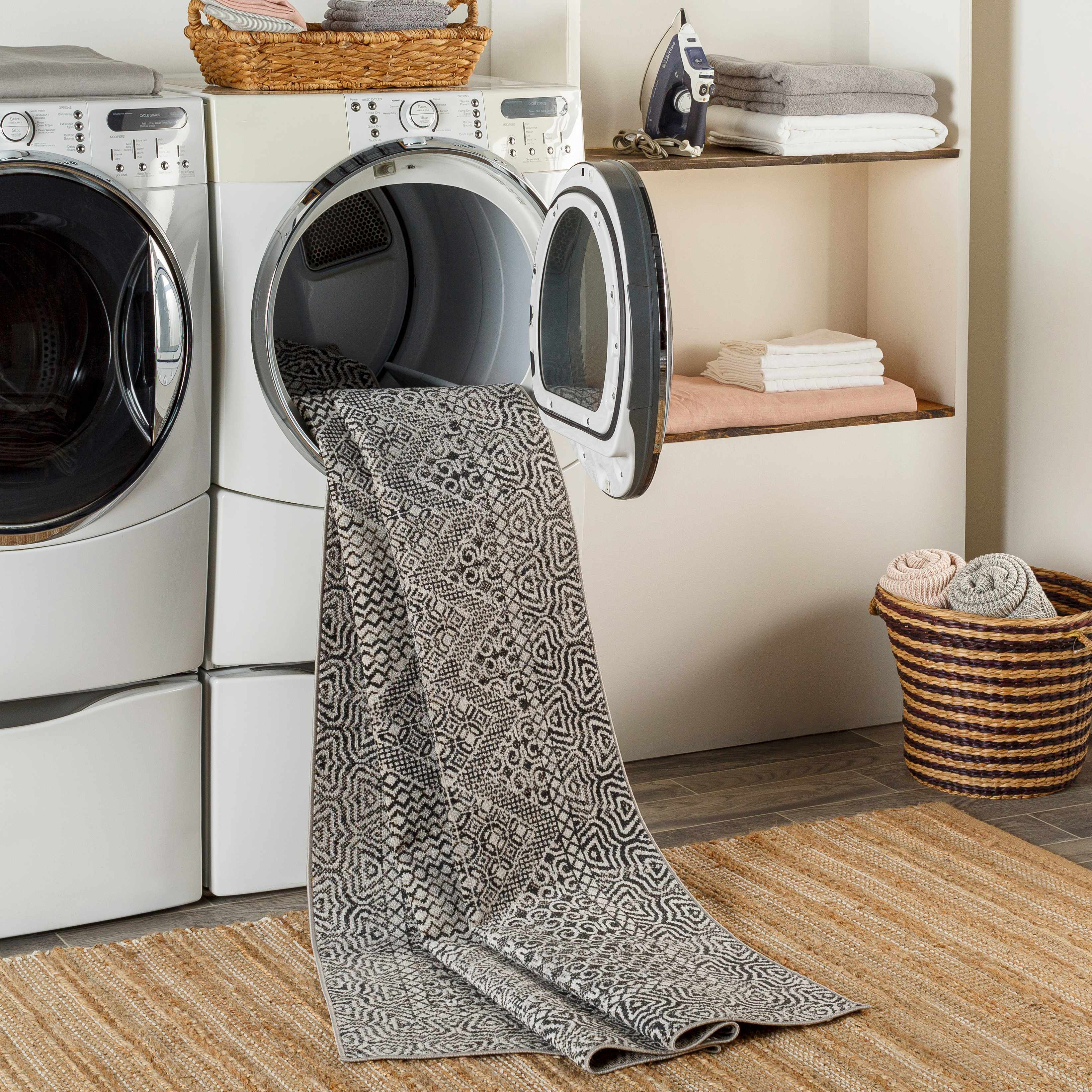 Laundry room scene with black and gray Consuelo Washable Area Rug coming out of the dryer on top of a jute rug. Washing-Machine