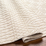 Close-up of the Ryne Area Rug showing its white thatch color, hand-woven texture, and bohemian diamond pattern. Fold