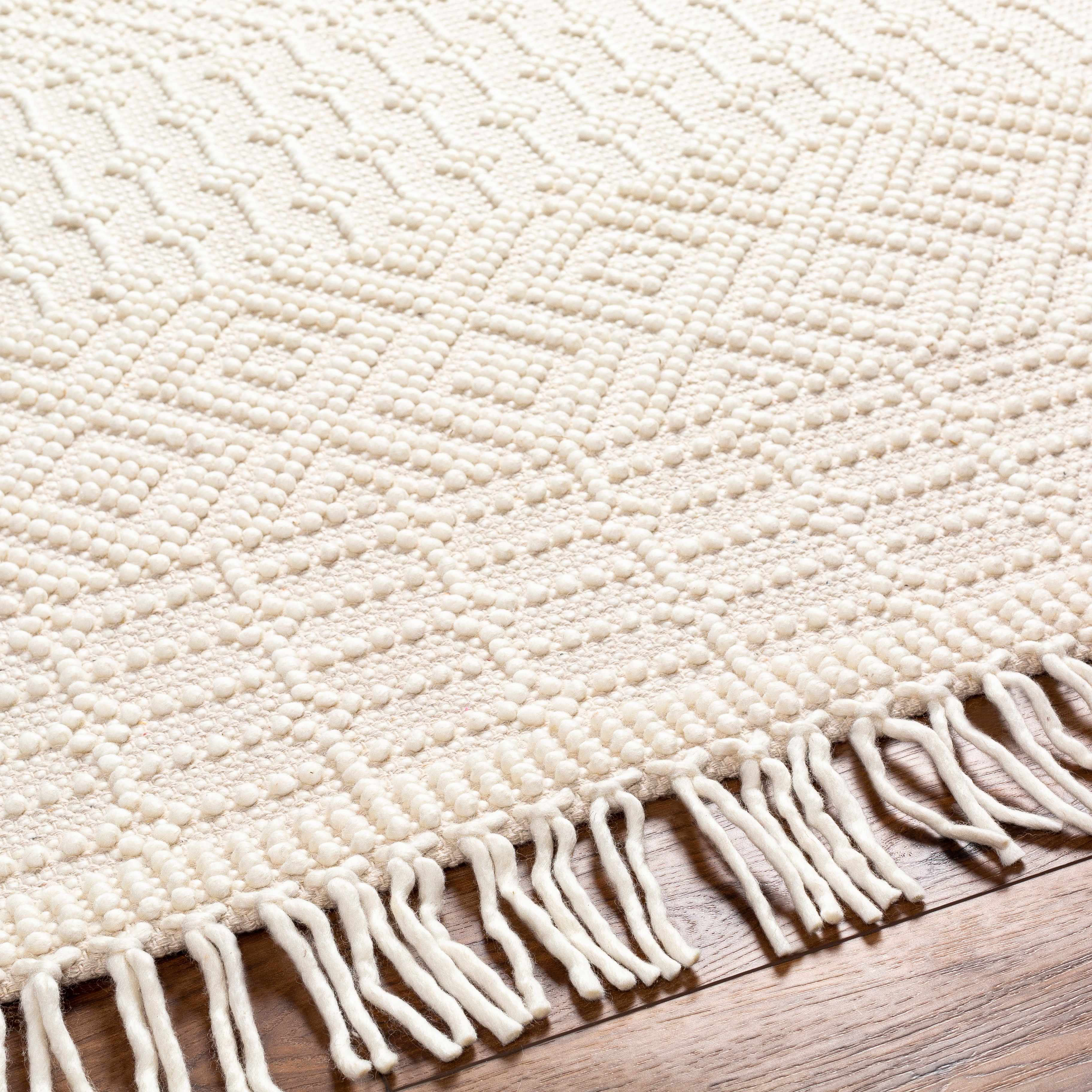 Close up of the Ryne Area Rug showing the white thatch color, geometric pattern, woven texture, and fringe. Texture