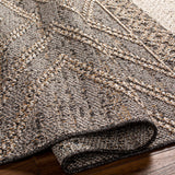 Close-up of the Beige Charcoal Areli Area Rug showing geometric patterns and textured weave with black, mustard, and taupe colors. Fold