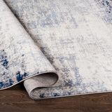 Close-up of the Texanna Abstract Blue/Gray Area Rug showing its light blue, gray, and off-white abstract design. Fold