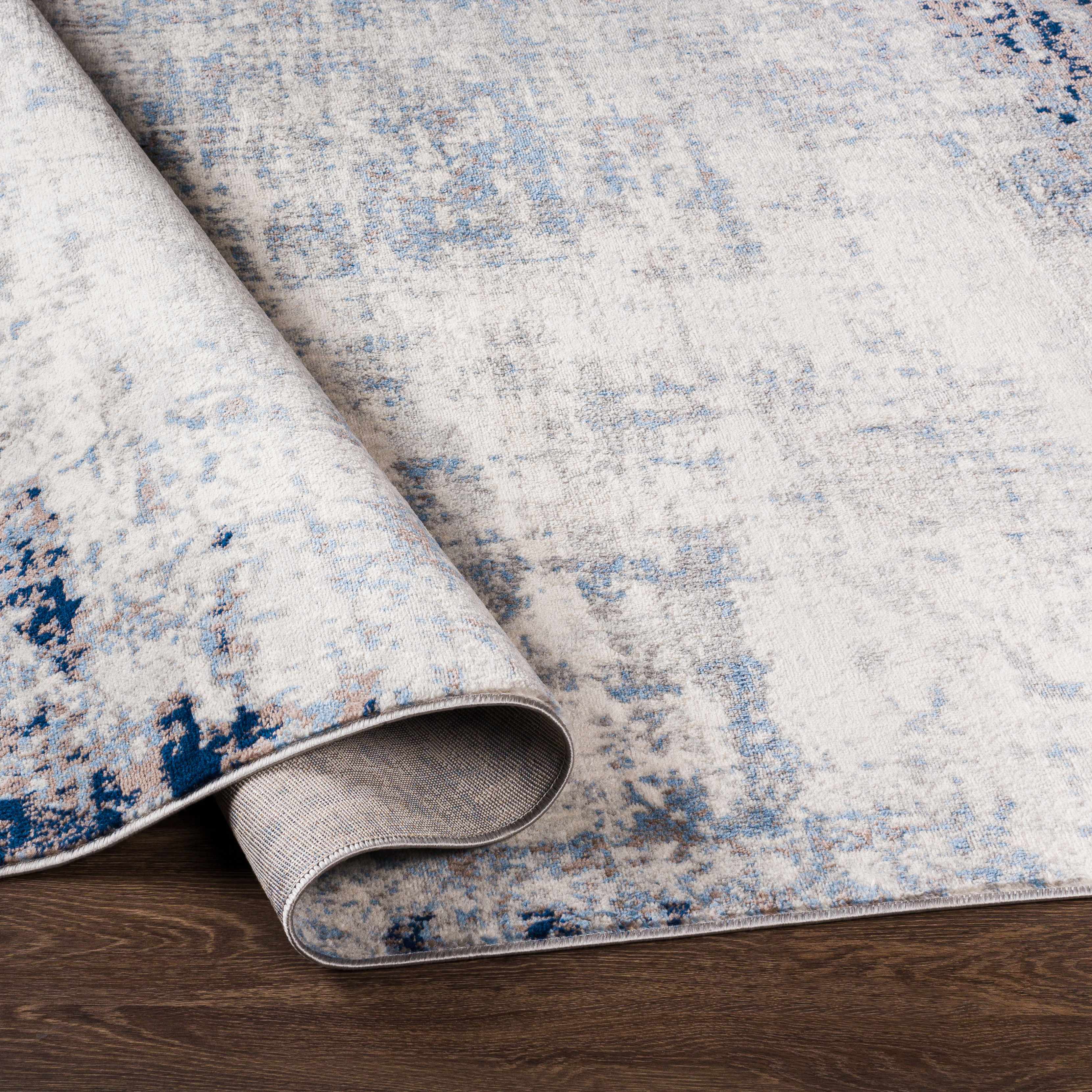 Close-up of the Texanna Abstract Blue/Gray Area Rug showing its light blue, gray, and off-white abstract design. Fold