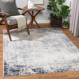 Living room scene with a Texanna Abstract Blue/Gray Area Rug, wood chair, side table, and potted plant on a wood floor. Roomscene-Rectangle