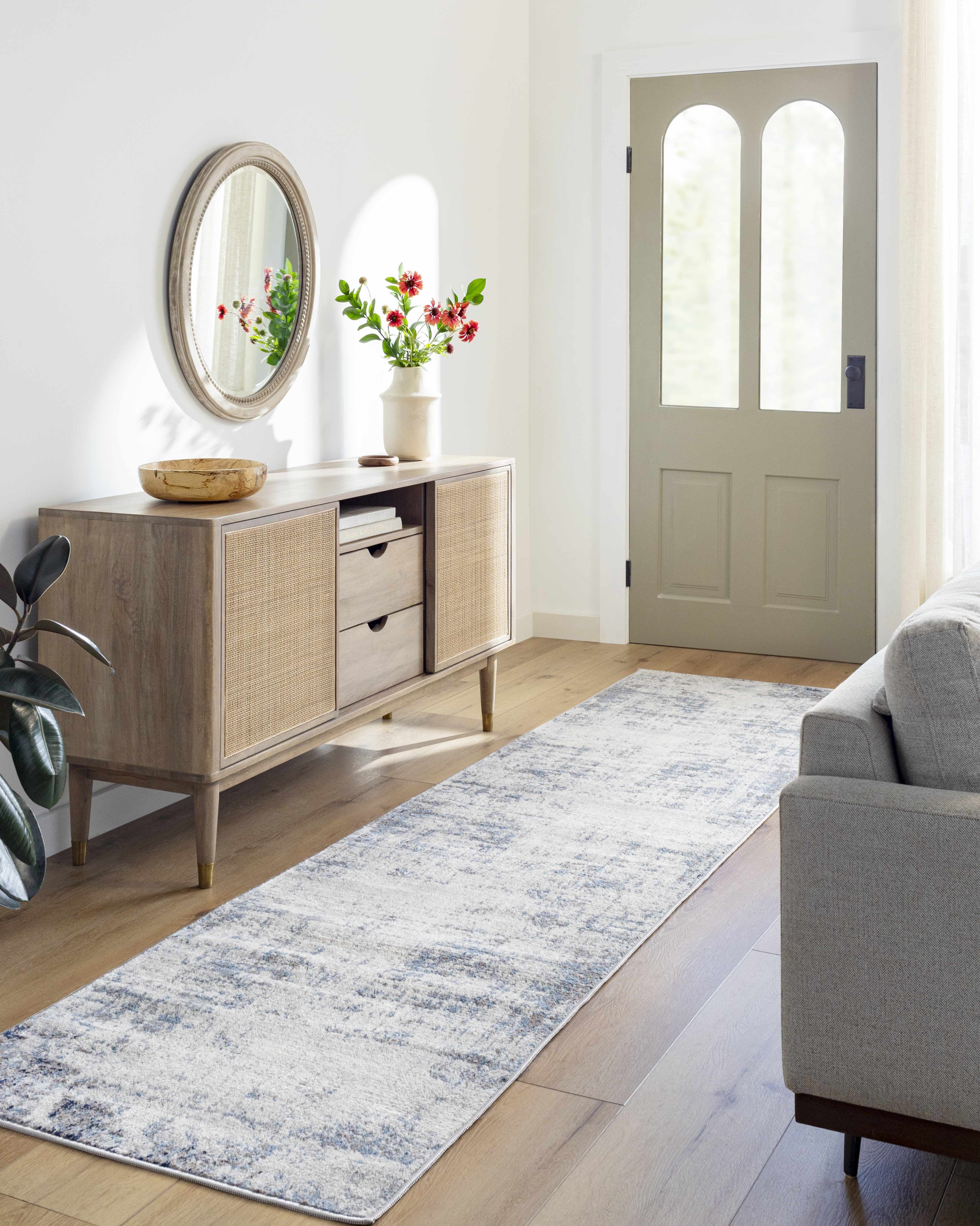 Entryway with a Texanna Abstract Blue/Gray Area Rug runner, wood floors, console table, mirror, and gray sofa. Roomscene-Runner