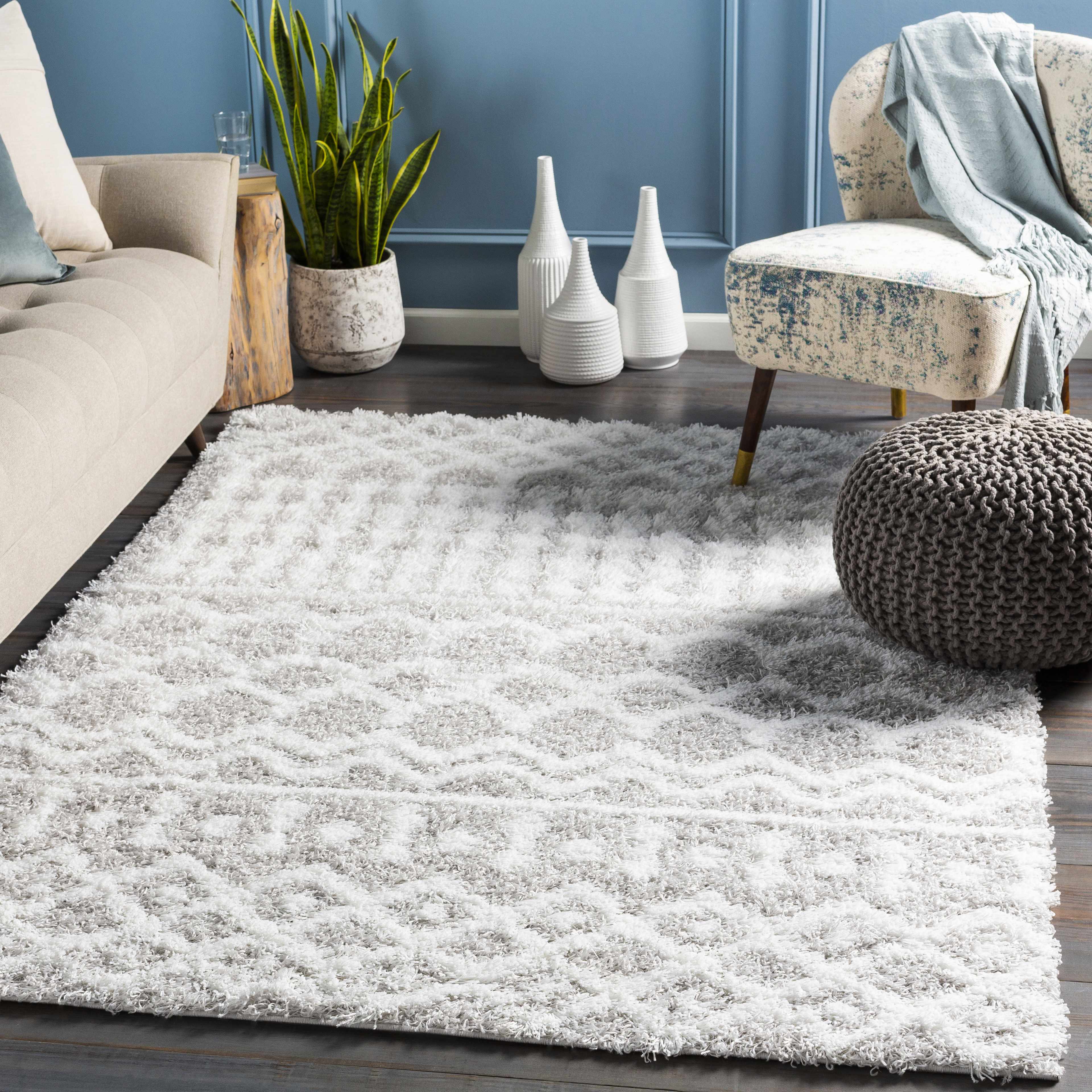 Living room scene with a light gray Vernonburg Shag Area Rug, beige sofa, patterned chair, and gray pouf on a dark wood floor. Roomscene-Rectangle